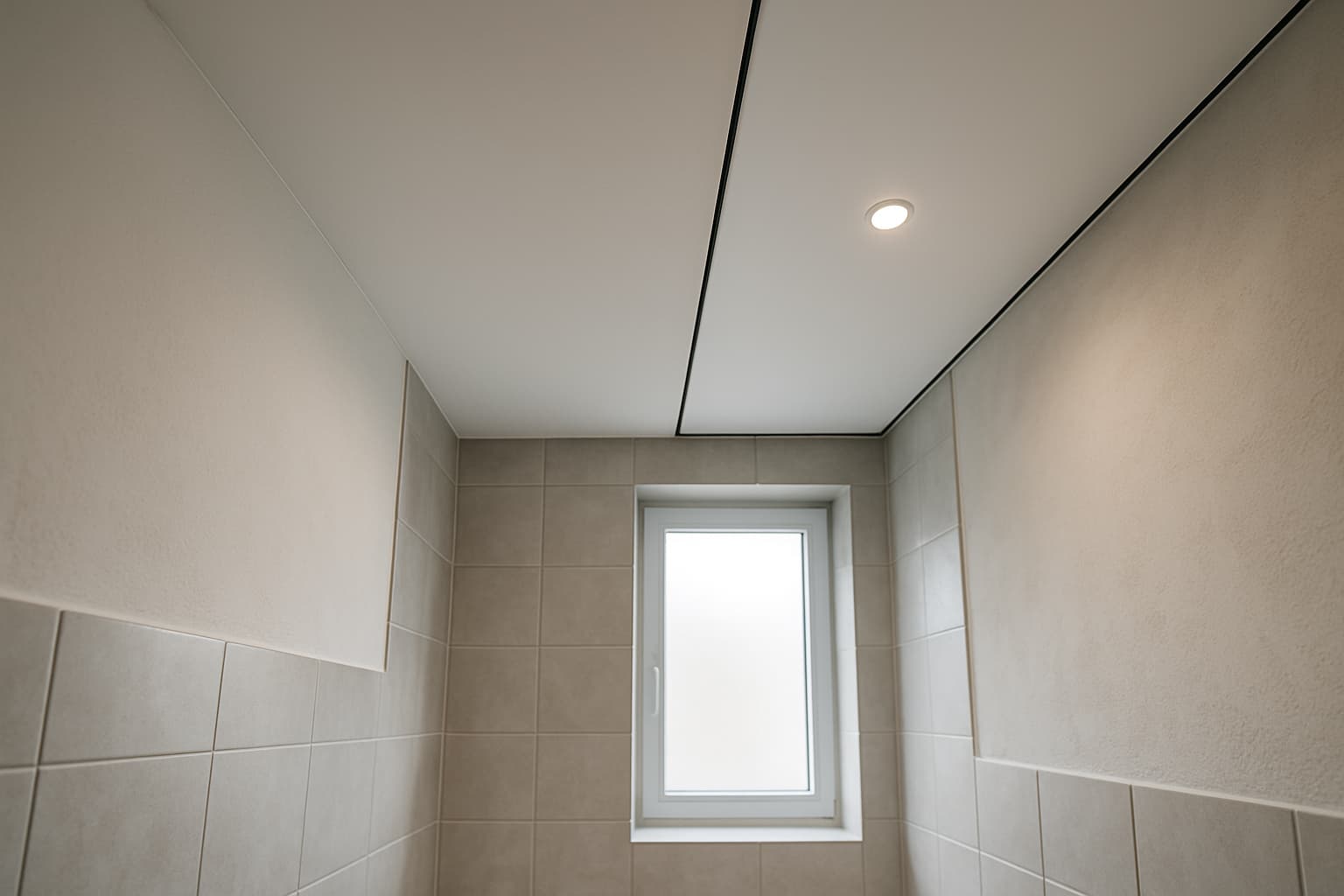 Moderne badkamer van onderaf gefotografeerd met een glad wit plafond en een gedeelte spanplafond met inbouwspot, daglicht via een matglazen raam