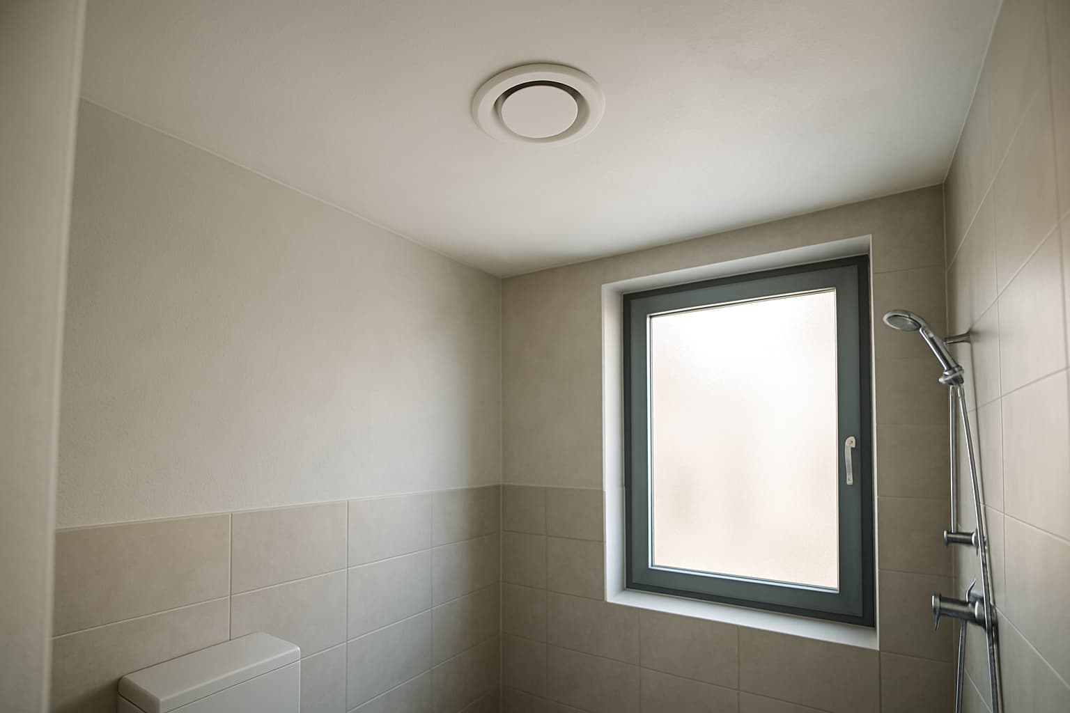 Strak gestuukt badkamerplafond met een rond ingebouwd ventilatierooster, verlicht door zacht daglicht
